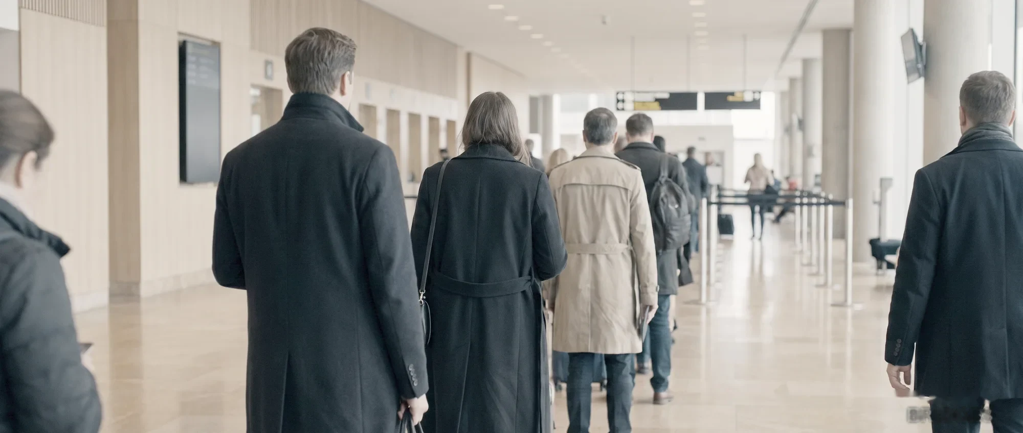 A passport control hall: travellers at the desks, seen from behind